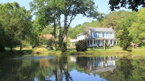 Ein großes Haus mit Veranda, umgeben von Bäumen und einem Teich.