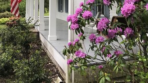 Eine Veranda mit weißen Säulen, einer aufgehängten amerikanischen Flagge und rosa Blumen.