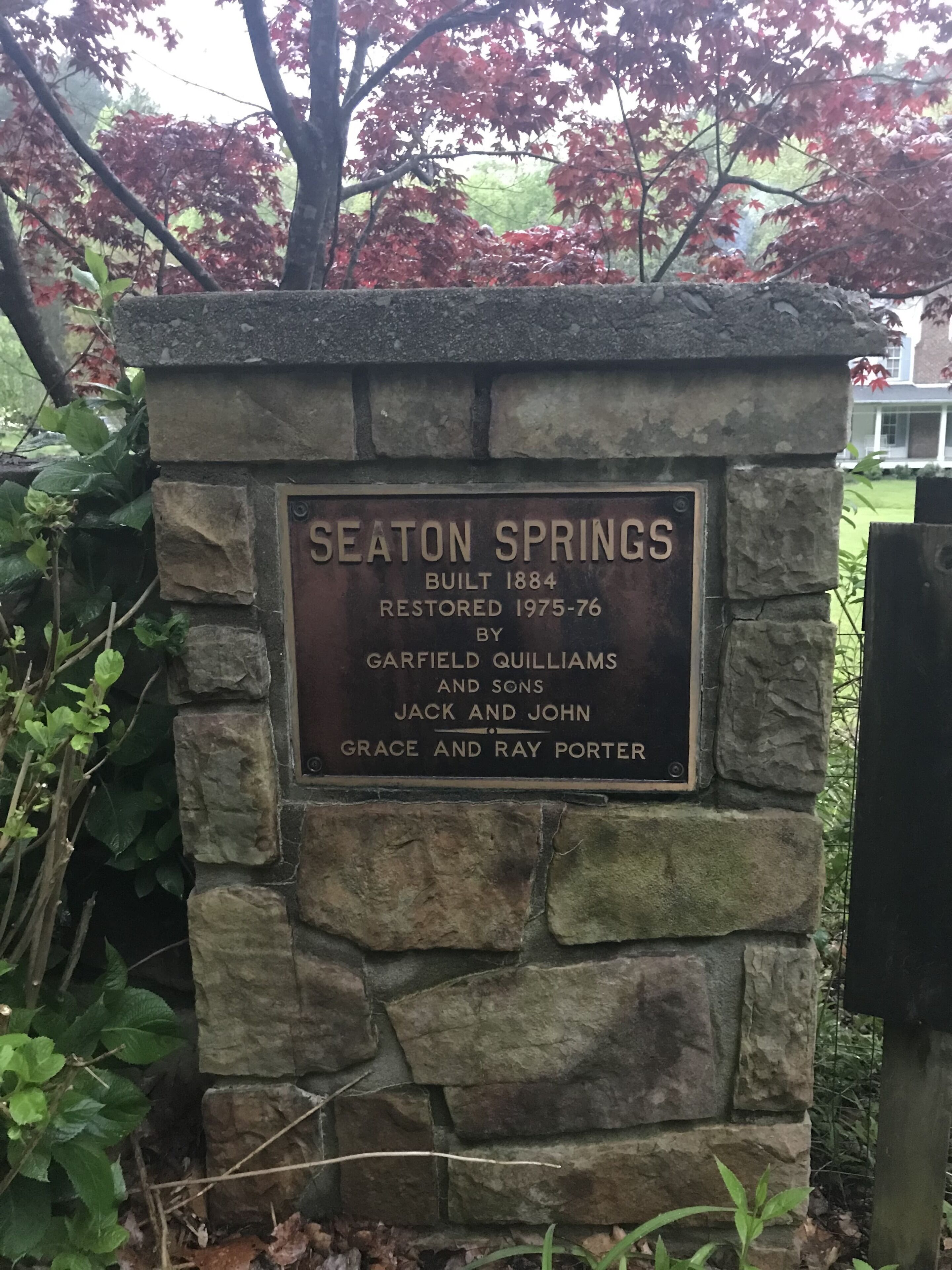 Un mur de pierre sur lequel est fixée une plaque portant l’inscription suivante : « SEATON SPRINGS, CONSTRUIT EN 1884, RESTAURÉ DE 1975 À 1976 PAR GARFIELD QUILLIAMS ET FILS, JACK ET JOHN GRACE ET RAY PORTER ».