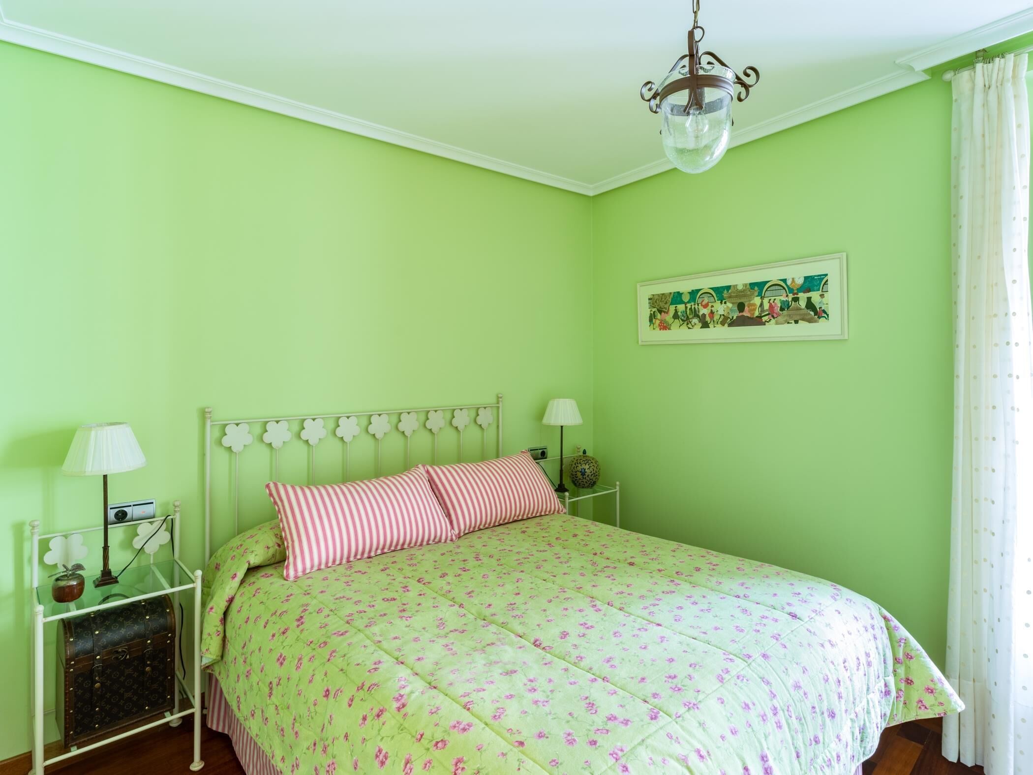 Une chambre avec un lit, deux tables de chevet, un luminaire suspendu et un tableau accroché au mur.