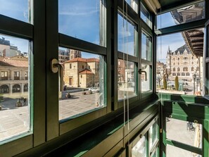 A view from inside a building with large windows overlooking a historic town square with buildings and a church. - Housing León- The Galery (León)