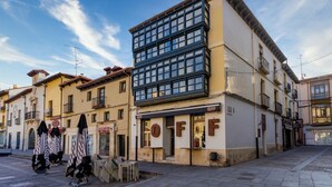A building with a ground-floor shop labeled "OFF" and a multi-story structure with large windows. - Housing León- The Galery (León)