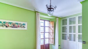 A room with green walls, a wooden floor, a bed with a floral bedspread, a hanging light fixture, and a door with glass panels. - Housing León- The Galery (León)