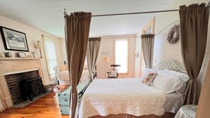 A bedroom with a four-poster bed, a fireplace, and a view of the outdoors.
