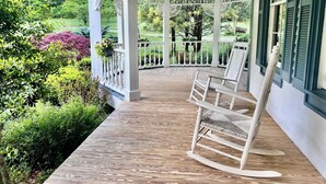 A covered porch with a wooden floor, white railings, and a rocking chair.