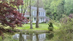 A house with a pond in front, surrounded by trees and a lawn.