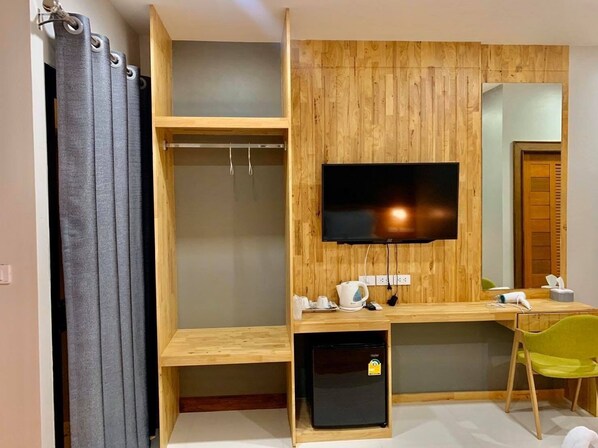 A compact room with a wooden desk, a television mounted on the wall, a small refrigerator, and a green chair. - Add Ubon Hotel (Warin Chamrap)