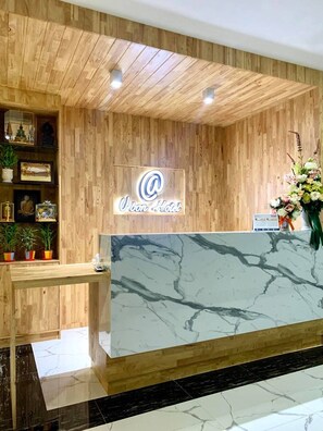 A hotel reception desk with a wooden panel wall, a marble counter, and a neon sign. - Add Ubon Hotel (Warin Chamrap)