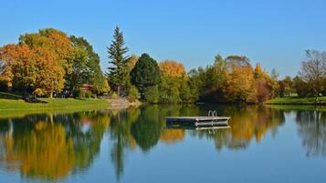 A calm lake with a dock, surrounded by trees with autumn foliage, reflecting the scenery.