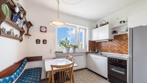 Una cocina con mesa, sillas, un banco, un reloj, una ventana y una estufa.