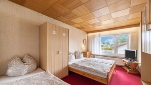 Un dormitorio con dos camas, un armario de madera, un escritorio con televisor y una ventana con vistas a zonas verdes.