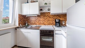 Cocina con armarios blancos, estufa, horno, pileta y ventana.