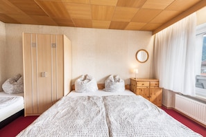 A hotel room with a bed, a wardrobe, a bedside table, a mirror, and a window with curtains.