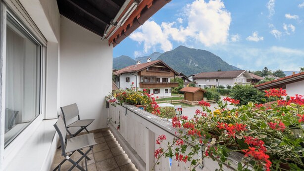 Un balcón con sillas, vista a casas y montañas al fondo.