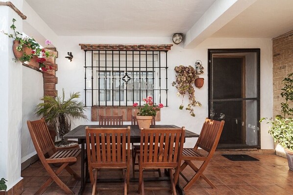 A patio with a table and chairs, a window with bars, and potted plants.