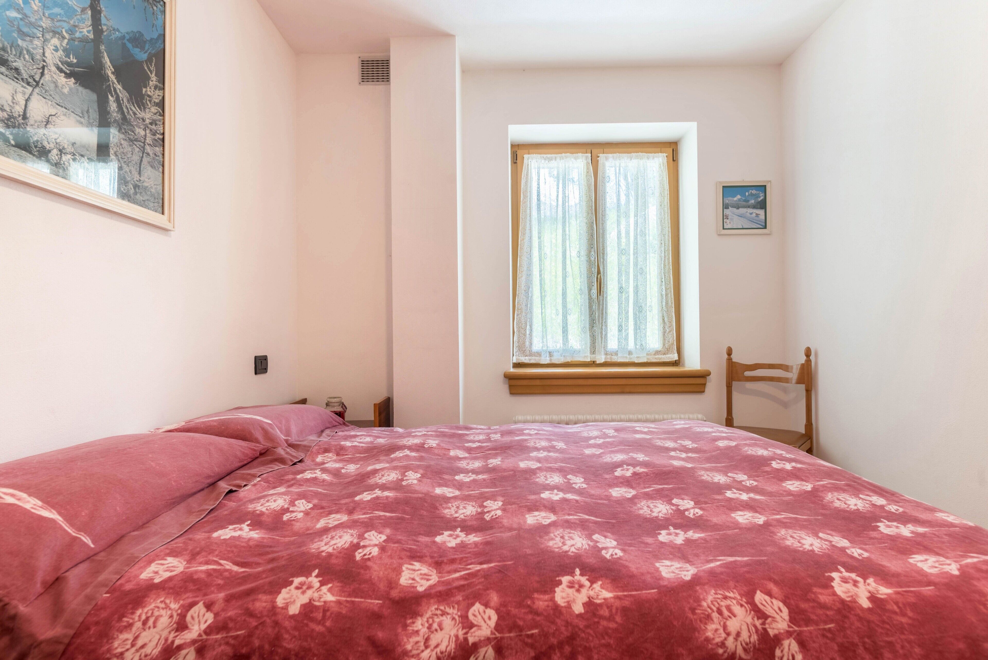 Ein Schlafzimmer mit Bett, Vorhängen am Fenster, einem Sessel und einem Bild an der Wand.