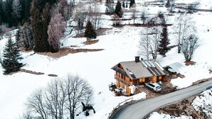 Eine Holzhütte mit geneigtem Dach, umgeben von schneebedecktem Boden und Bäumen.