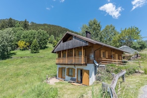 Eine Holzhütte mit Balkon, umgeben von einer Wiese und Bäumen.