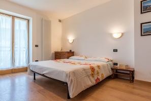 A bedroom with a bed, wooden floor, a nightstand, a dresser, and a window with curtains.