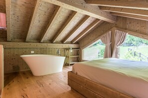 Une cabane en bois avec une grande baignoire, un lit et une fenêtre avec des rideaux.