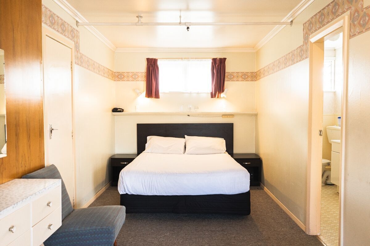 A bedroom with a bed, bedside tables, a dresser, a window with curtains, and a door.