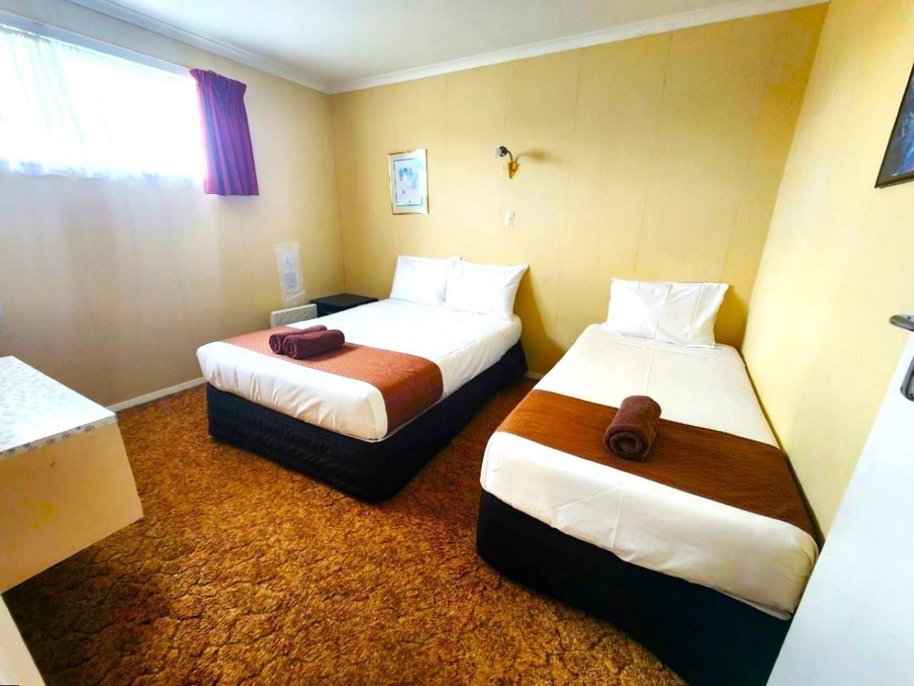 A hotel room with two beds, a desk, and a window with curtains.