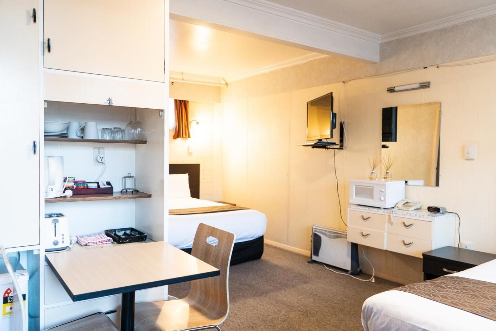 Habitación de hotel con cama, escritorio con silla, kitchenette pequeño, cómoda y televisor.