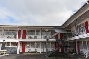 A two-story building with a red and white facade, multiple balconies, and a staircase leading to the upper floor. - Mayfair Court Motel (Tokoroa)