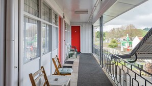 Un balcon donnant sur la ville, une porte rouge et une rangée de chaises.