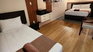 Une chambre d’hôtel avec un grand lit, un lit plus petit, une télévision, une commode et un miroir.