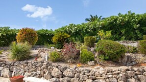 Ein Garten mit einer Steinmauer, einer weißen Bank und Topfpflanzen.