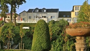 A landscaped garden with a fountain, a neatly trimmed hedge, and a building with a sign that reads 'TERBASSER-KAFFE' in the background. - Ferienwohnung 2 mit Meerblick und Südbalkon (Heringsdorf)