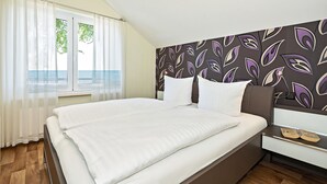 A bedroom with a bed, a nightstand, a window with curtains, and a patterned wall. - Ferienwohnung 2 mit Meerblick und Südbalkon (Heringsdorf)