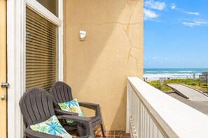 A balcony with two chairs, a view of the ocean, and a sign indicating a beach access point.