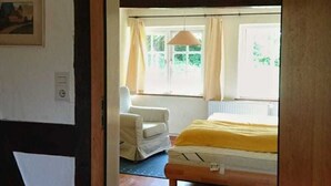 Una habitación con cama, una silla, una ventana con cortinas y una lámpara colgante.
