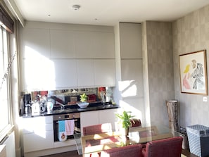 A modern kitchen with white cabinets, a glass dining table, and a red sofa. - Notting Hill designer apartment (London)