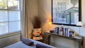 Une chambre à coucher bien rangée, avec un lit, une table de chevet sur laquelle sont posés des livres, une lampe et une fenêtre avec des rideaux.