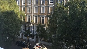 Une rangée de maisons mitoyennes aux fenêtres à cadre blanc et aux façades en briques, entourées d’arbres.