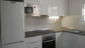 Een moderne keuken met witte kasten, een ingebouwde magnetron, een fornuis en een koelkast.