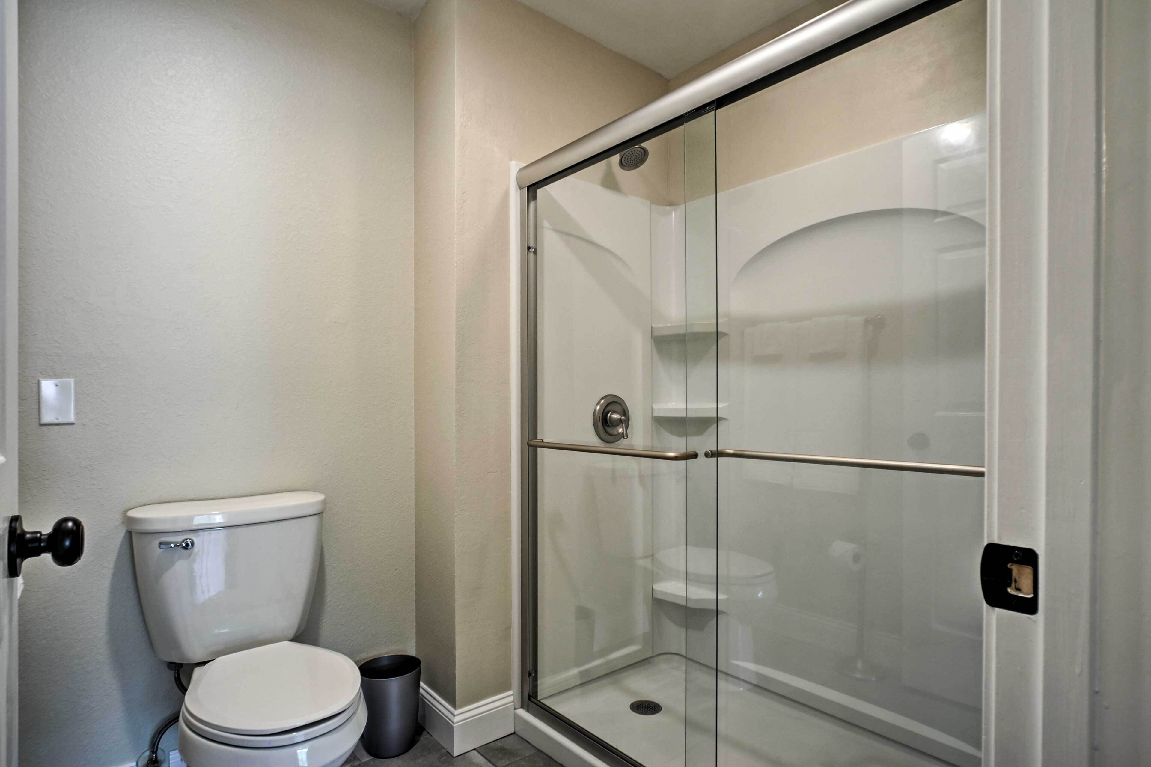 A bathroom with a toilet, a glass-enclosed shower, and a trash can.
