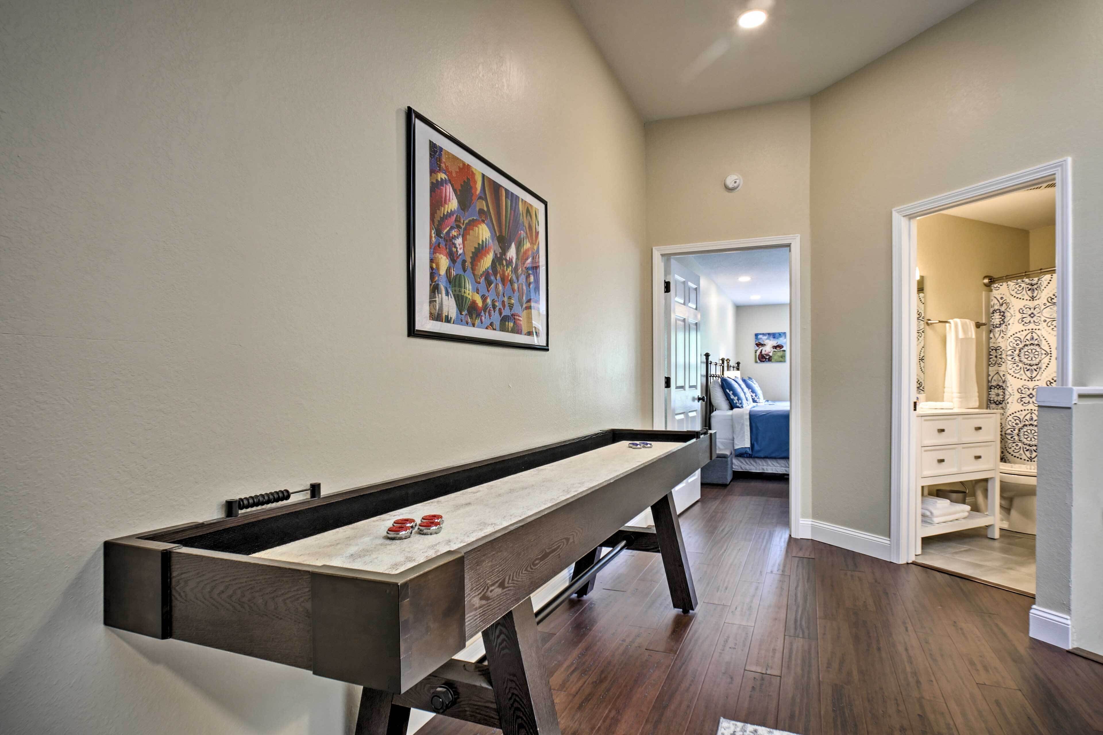 A room with a pool table, a framed abstract painting, and a hallway leading to a bathroom with patterned curtains.