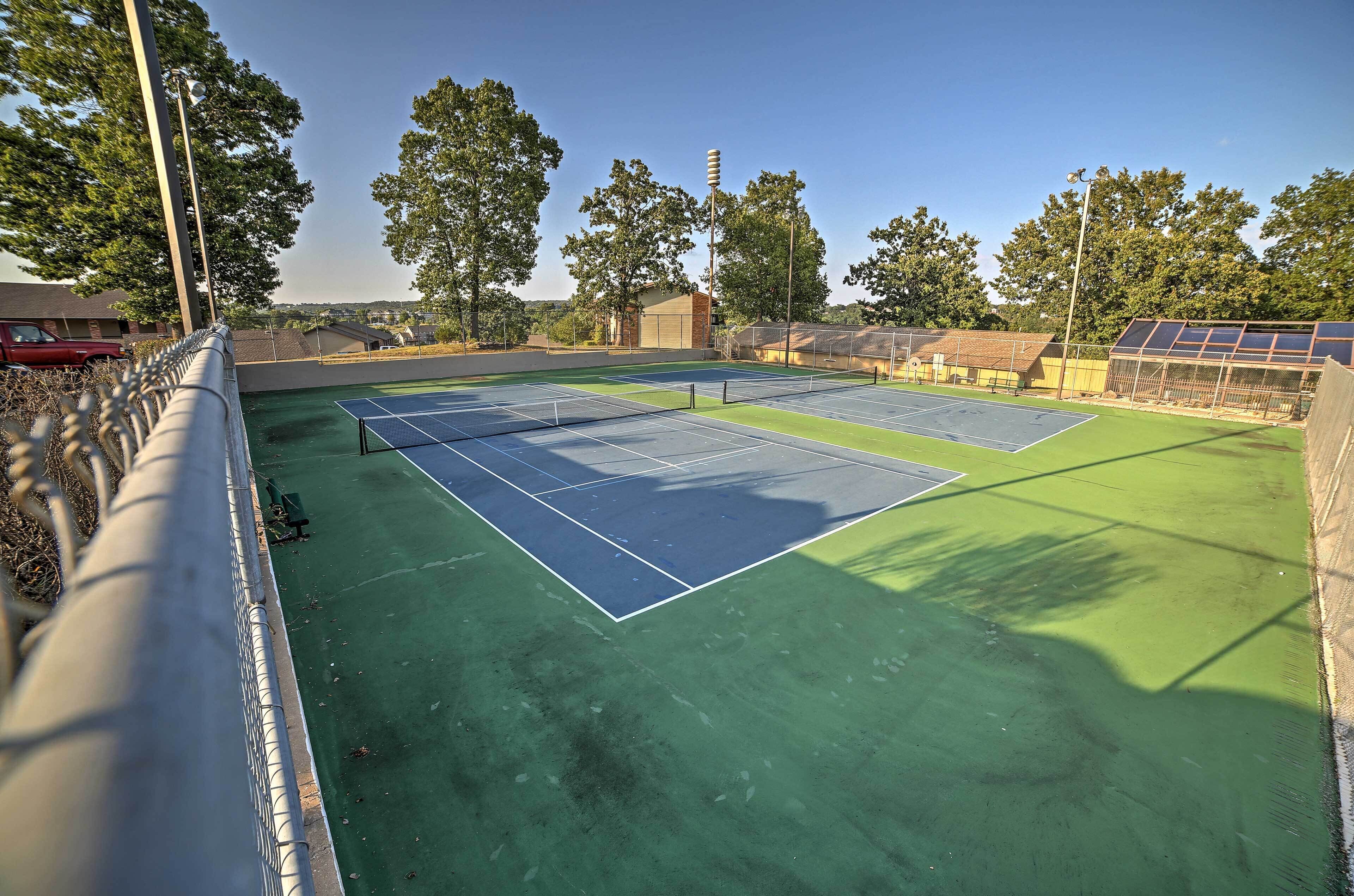 Un court de tennis extérieur doté d’une surface verte, entouré d’arbres et d’une clôture.