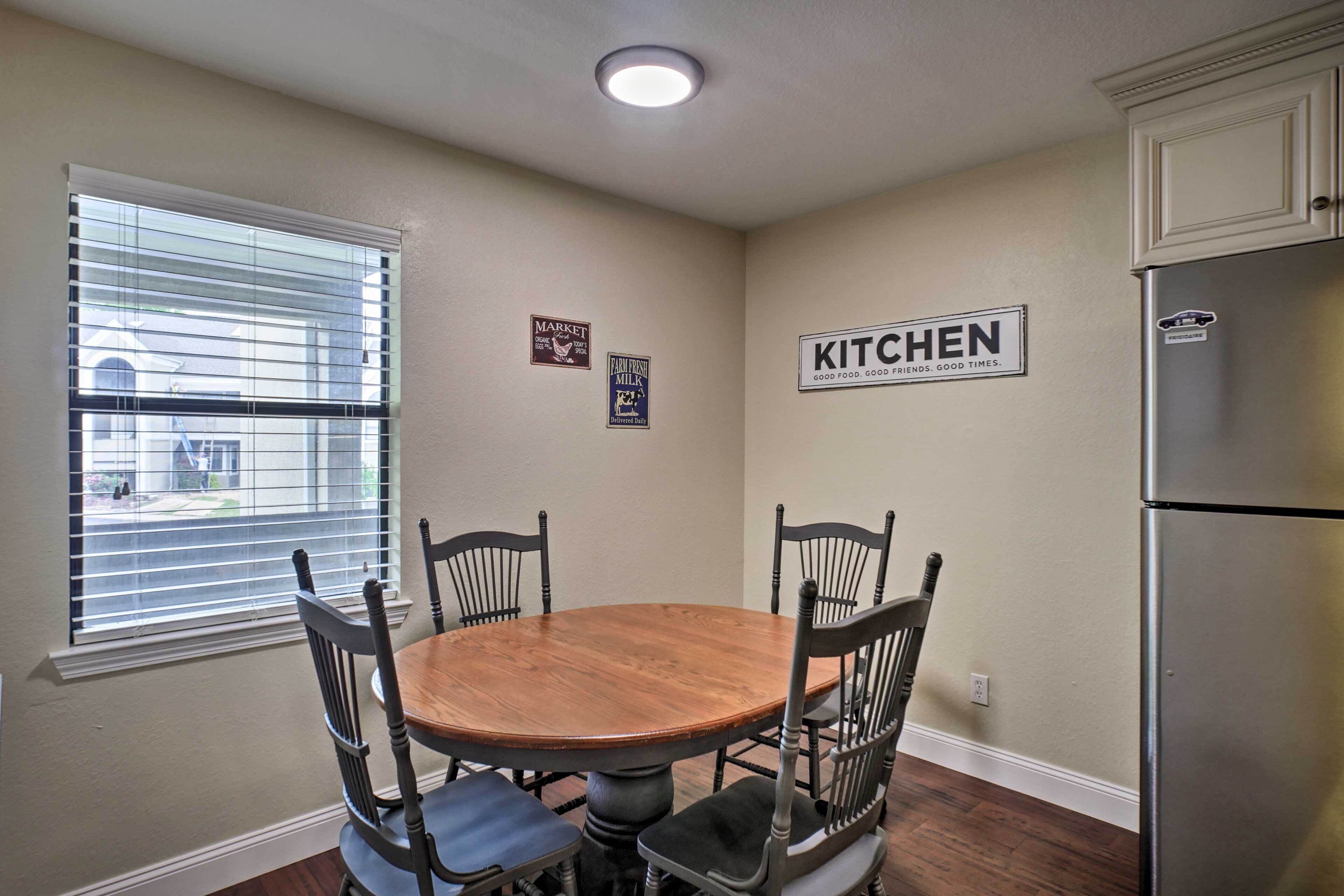 A dining area with a wooden table and four chairs, a refrigerator, and a window with blinds.