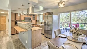 A modern kitchen with a central island, stainless steel appliances, and a dining area with a view of the outdoors. - The Overlook Gem: Stunning Views & Serenity Awaits (Nine Mile Falls)
