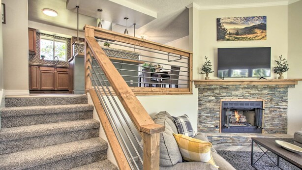 A staircase with wooden railings, a stone fireplace, a flat-screen TV above the fireplace, and a dining area with a table and chairs. - The Overlook Gem: Stunning Views & Serenity Awaits (Nine Mile Falls)