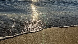 A beach with sunlight reflecting off the water, a sandy shore, and a distant city skyline. - A truly exceptional villa (Xàbia)