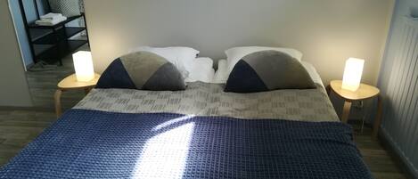 A bed with a blue textured cover, two bedside tables with lamps, and a wall-mounted rack with hangers.