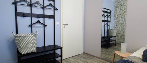 A bedroom with a bed, a mirror, a wardrobe with a hanging rack, and a small table with a basket.