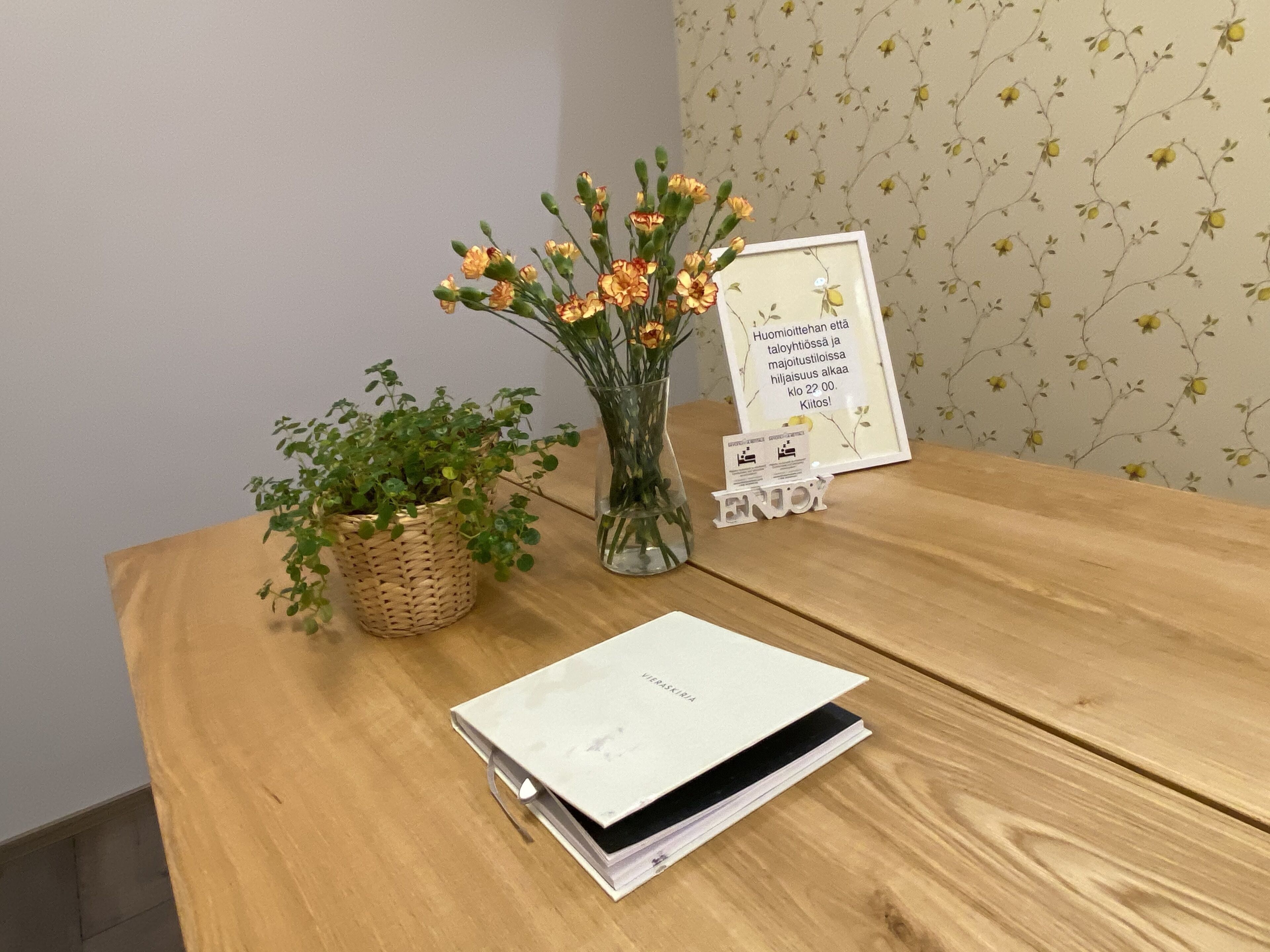 Ett träbord med ett vitt anteckningsblock, en vas med blommor och en inramad skylt.