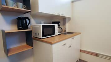 Una kitchenette compacta con microondas, cafetera y un estante con tazas.